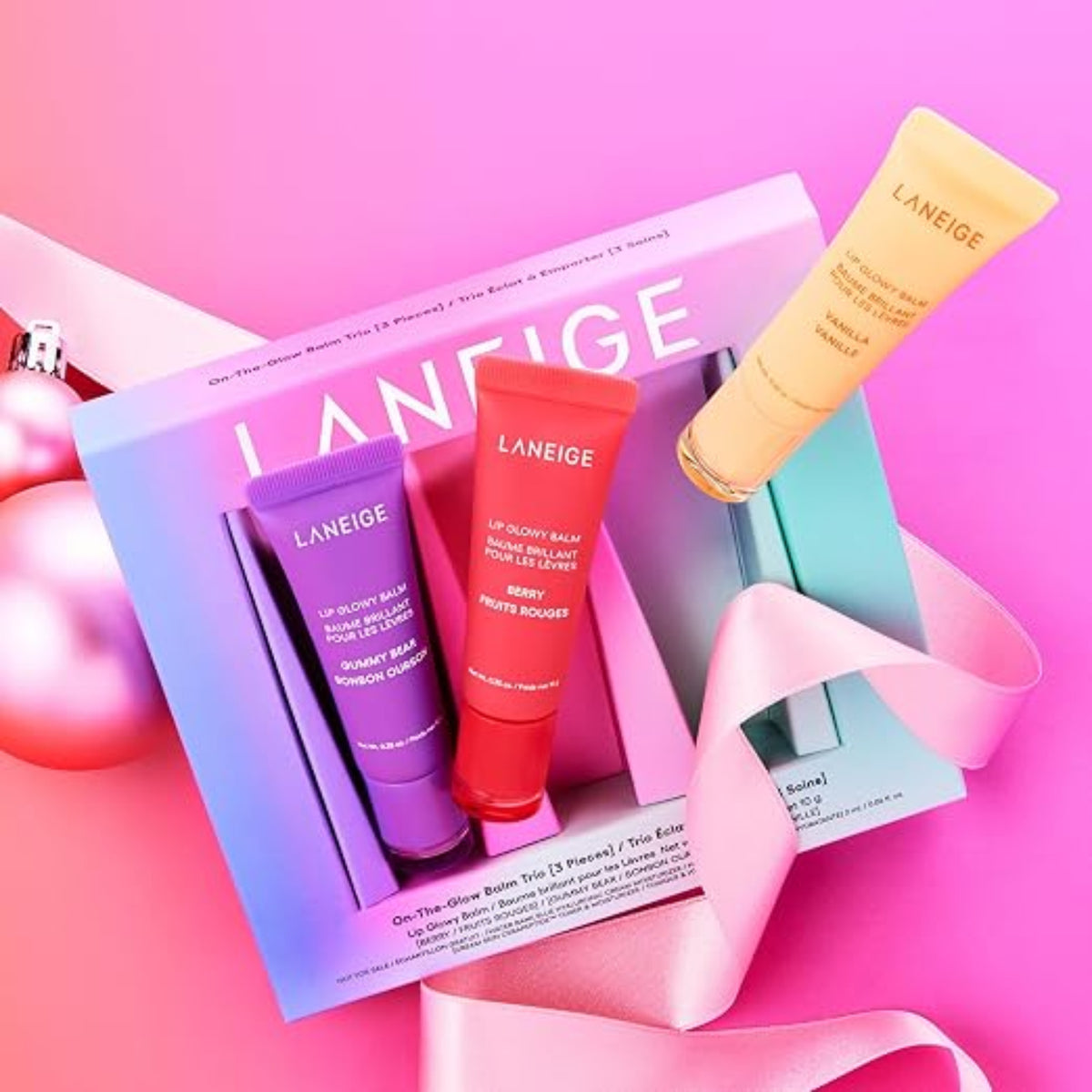 LANEIGE Lip Glowy Balm Trio Set with three tubes arranged around the gift box on a pink background.⠋