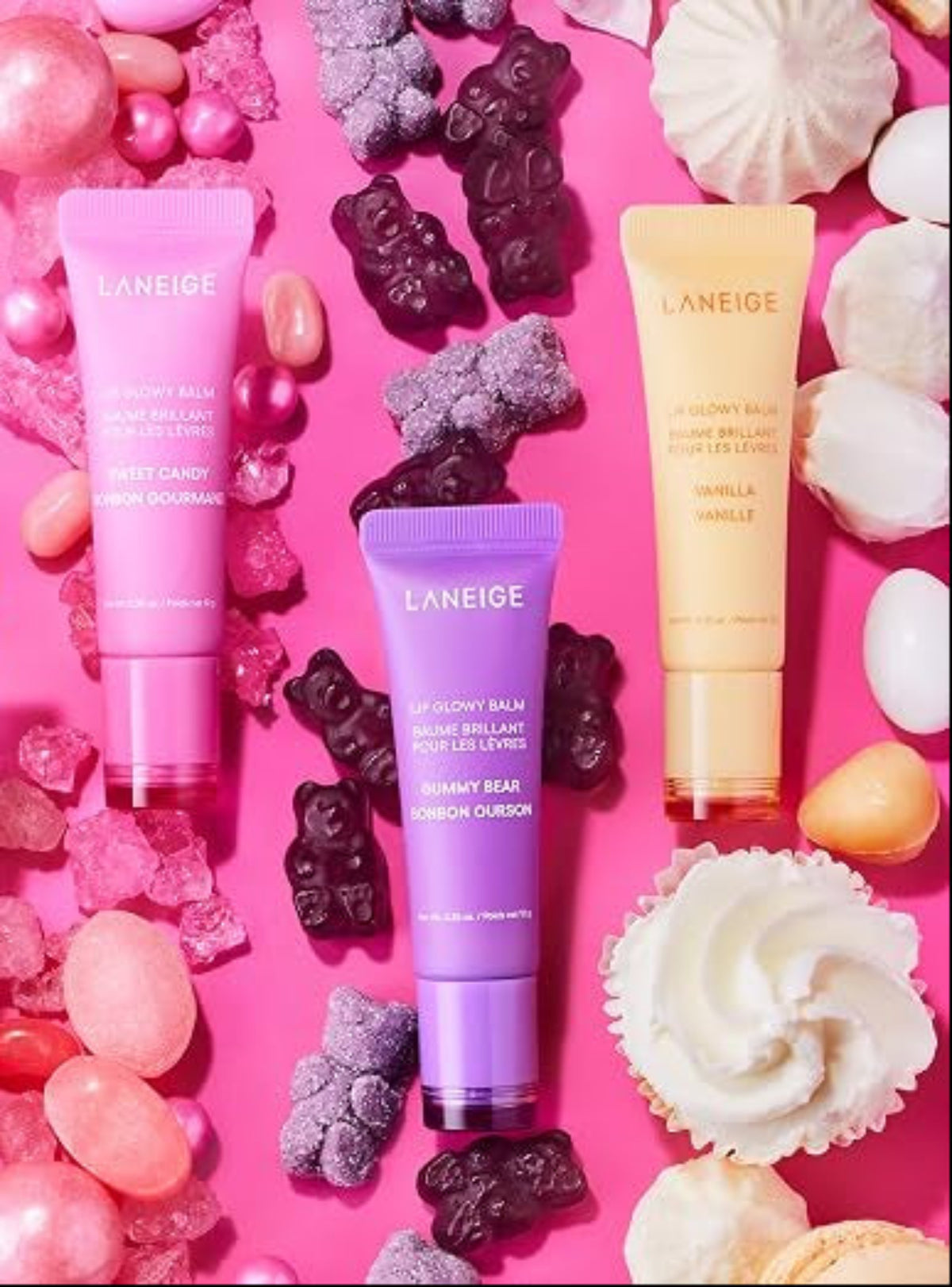 LANEIGE Lip Glowy Balms in Berry, Gummy Bear and Vanilla on a pink background with fruit and sweets.