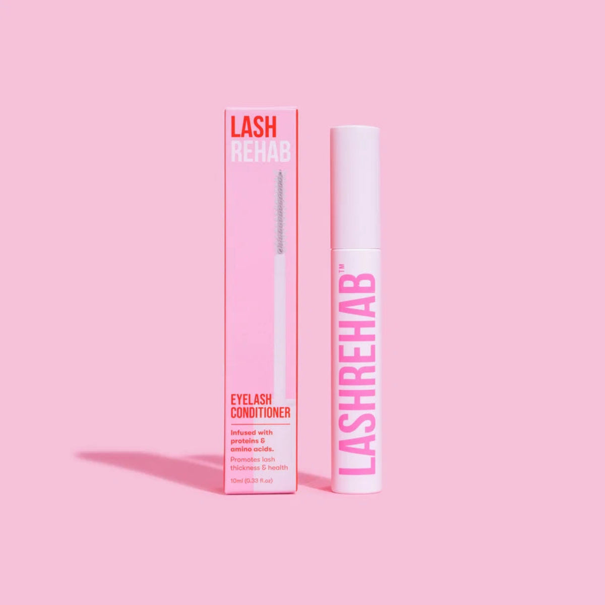 Lash Rehab Eyelash Conditioner shown with its pink retail box and white applicator tube on a solid pink background.