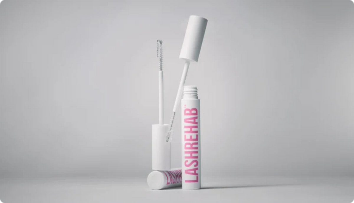 White Lash Rehab conditioner tube with pink lettering, shown with the wand and spoolie in a clean studio setup against a light gray background.